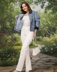 Woman in a denim jacket and white pants posing against a red background