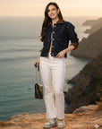 Woman in a denim jacket and white pants standing against a red background