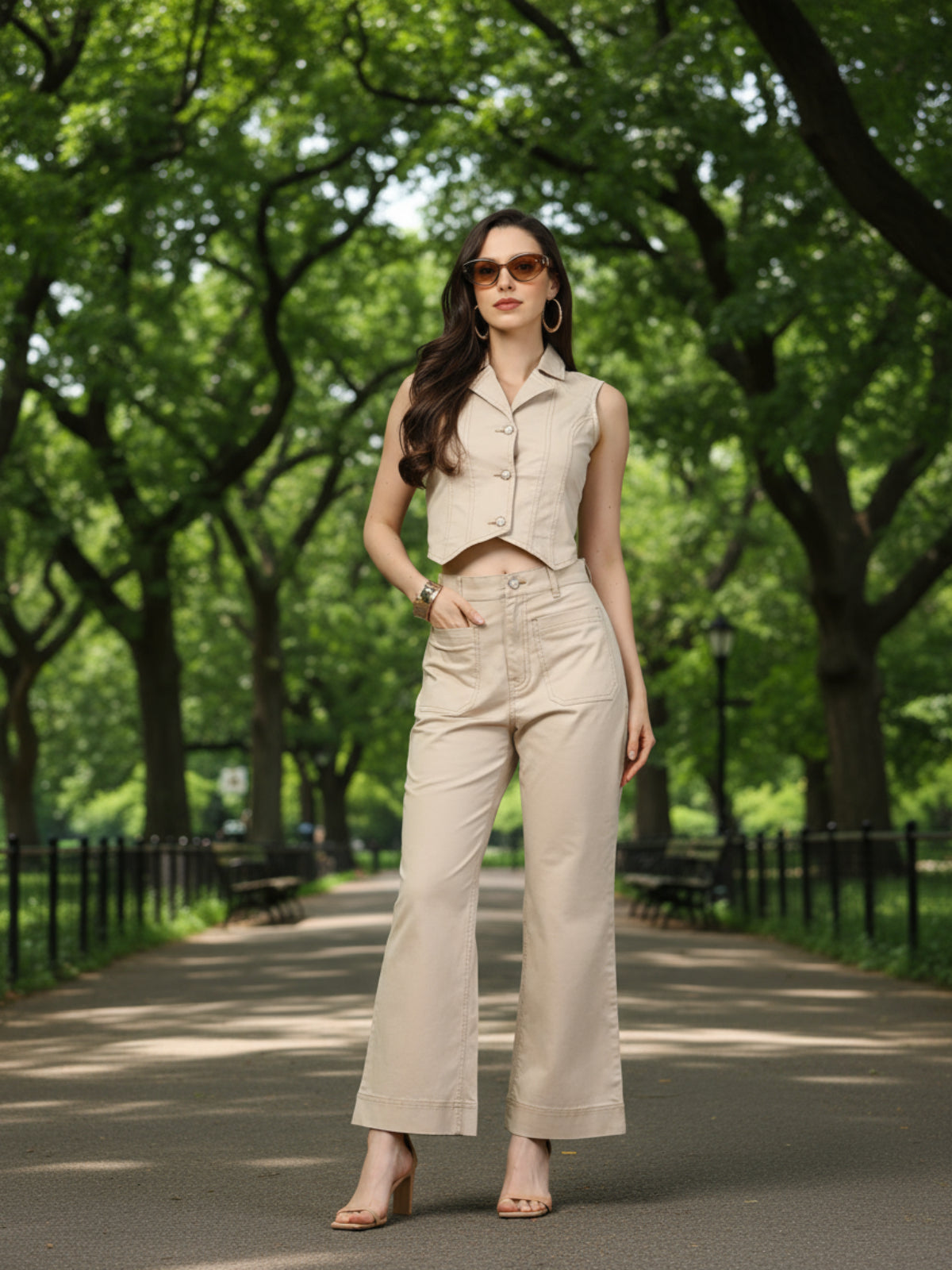 Woman in a beige outfit standing in a park with trees and pathways in the background
