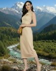 Woman in a beige dress standing in a scenic mountain landscape with a river.